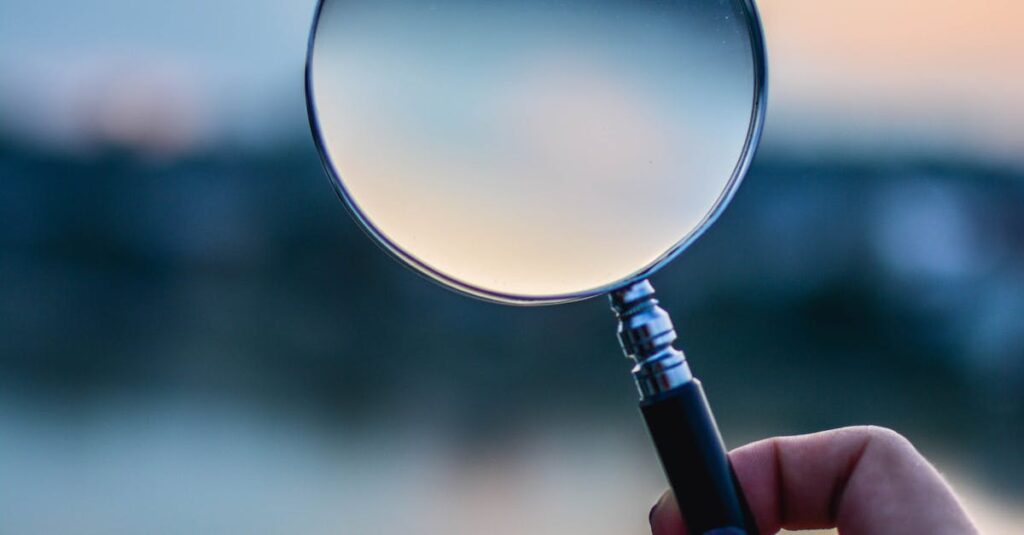A magnifying glass held by a hand outdoors at sunset, focusing on exploration.